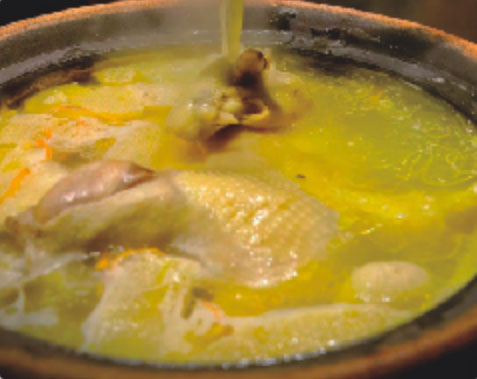 Traditional steaming chicken hotpot in a clay pot with fresh mushrooms and herbs in golden broth